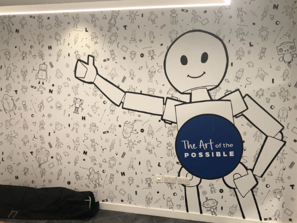 A photograph of the wall of a meeting room in the Hilton offices, Glasgow. On the wall, there are lots of small, illustrated robots, and one large robot. On the large robot, it says, 'The Art of the Possible'